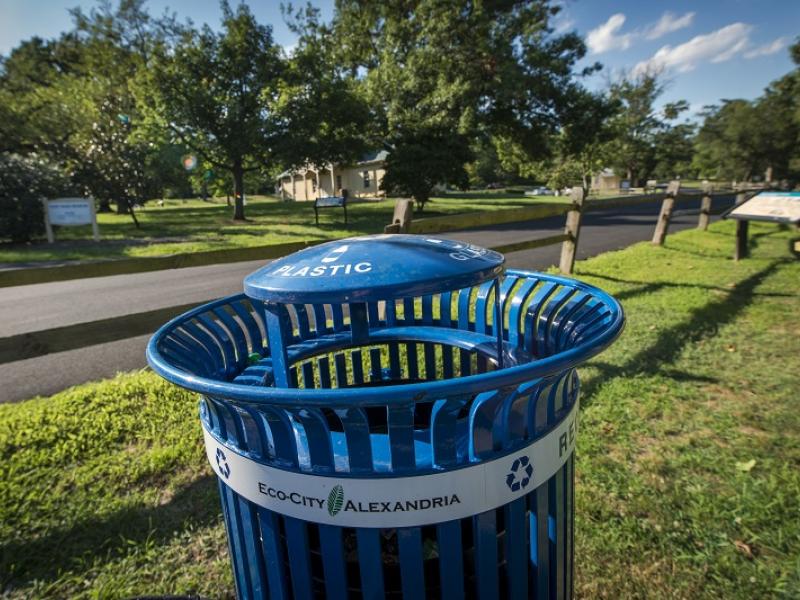 a photo of a blue, City-issues metal recycling can in an Alexandria park. "Eco-City Alexandria" sticker affixed to the front. 