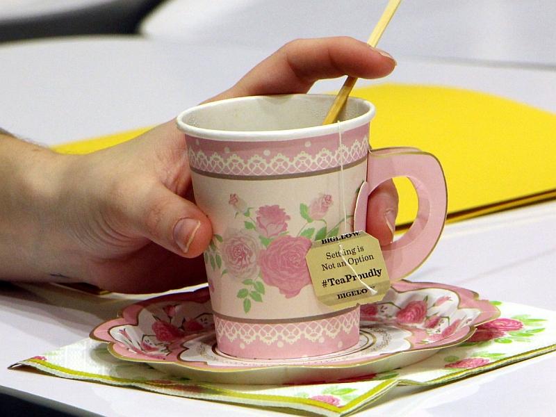 handling holding a cup decorated with flower with a tea bag tag visible